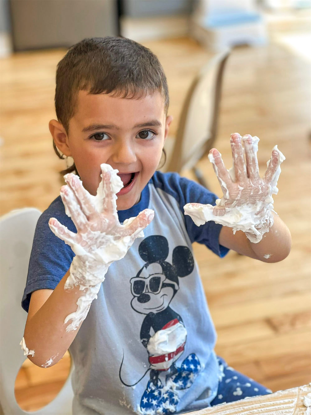 Young boy smiles with hands covered in white foam, showing them up in a craft activity.