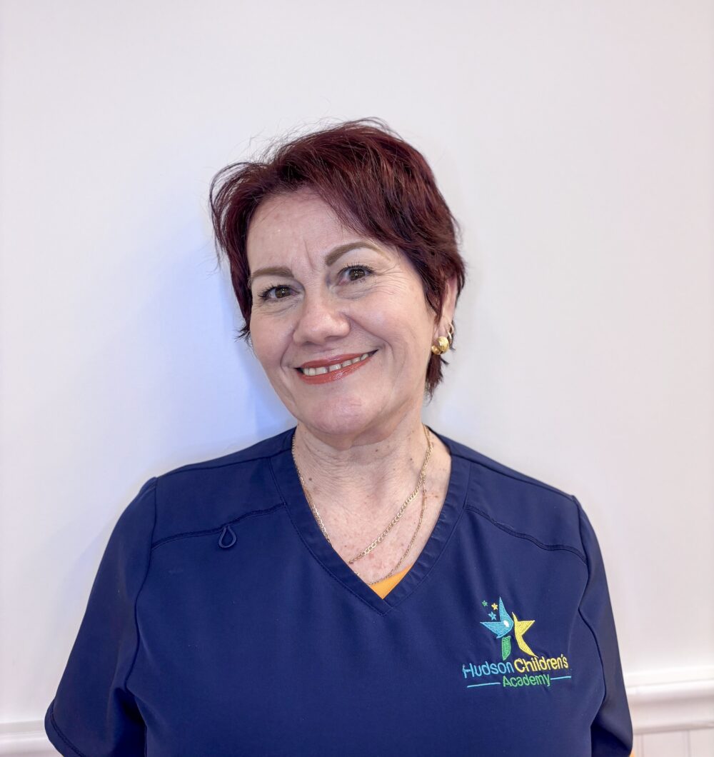 Smiling woman wearing navy scrubs with Hudson Children's Academy logo on the chest.